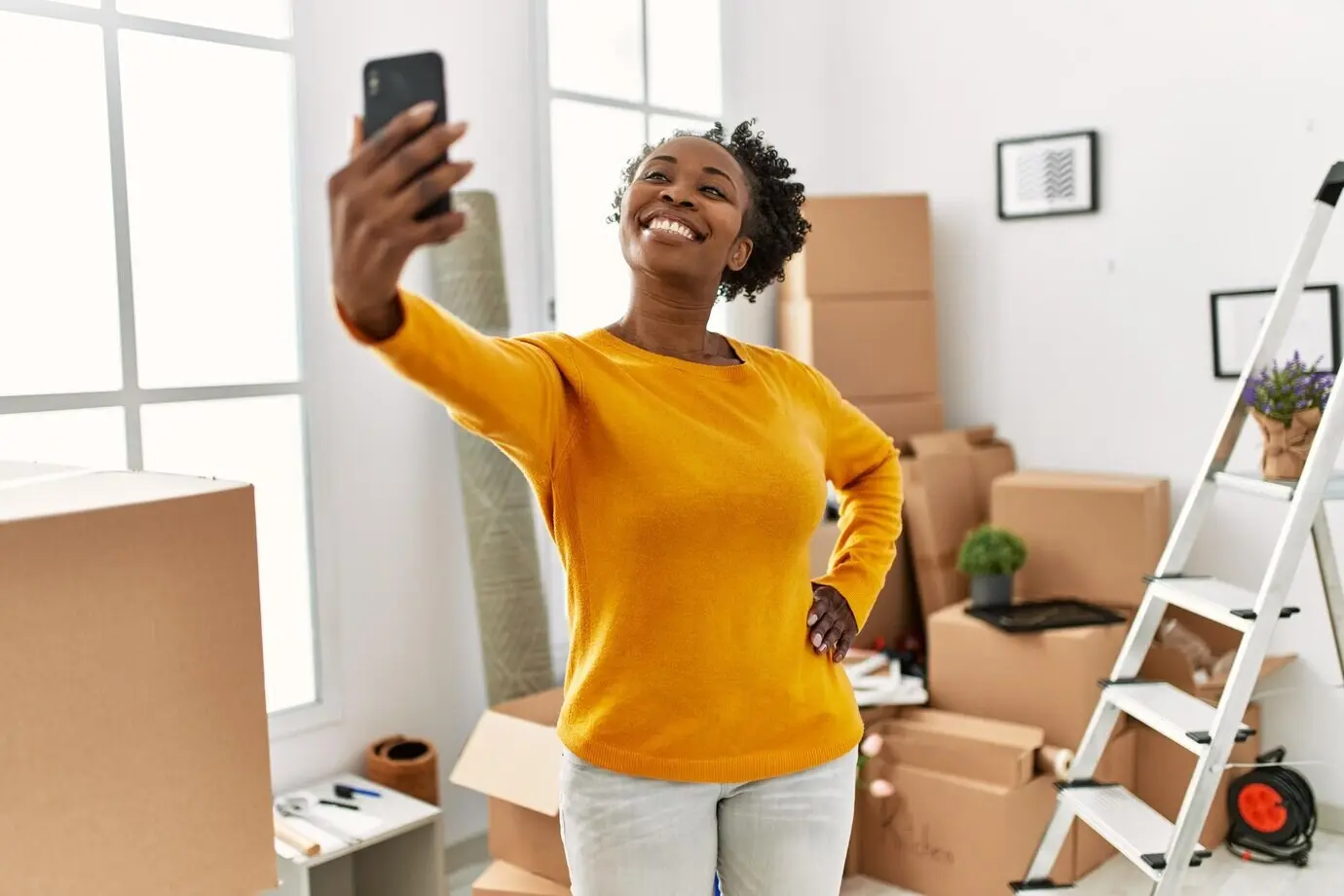An African American woman takes a selfie with a smartphone while standing at a new home.